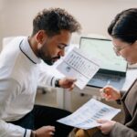 Man in White Long Sleeves Holding White Paper Discussing With Woman